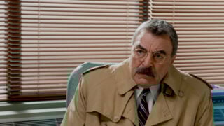 Frank wearing a trench coat and suit and tie and sitting in a green chair in someone's office on Blue Bloods Season 14 Episode 15